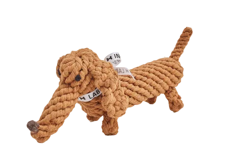 A rope-dog style dog toy made from thick tan rope, with a long snout, four legs, and a tail, shown on a plain white background. Small white tags with black text are attached near the neck and body.